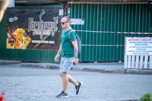 Фото мужчины с татуировкой на руке в готическом стиле на фоне городского пейзажа. Детализированный рисунок с аркой и деревьями, выполненный в черно-серых тонах. Пример стильного рисунка татуировки.
