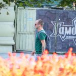Фото мужчины с татуировкой на руке в готическом стиле на фоне городского пейзажа. Детализированный рисунок с аркой и деревьями, выполненный в черно-серых тонах. Пример стильного рисунка татуировки.