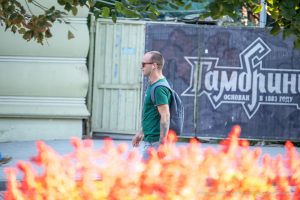 Фото мужчины с татуировкой на руке в готическом стиле на фоне городского пейзажа. Детализированный рисунок с аркой и деревьями, выполненный в черно-серых тонах. Пример стильного рисунка татуировки.