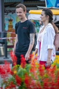 Фотография мужчины с татуировкой на предплечье, идущего рядом с девушкой. Татуировка выполнена в реалистичном стиле с изображением птицы и цветов.