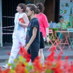 Фотография девушки с татуировкой на предплечье, идущей по улице. На заднем плане видны люди и яркие цветы.