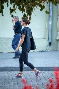 Фотография девушки с татуировкой на руке и плече, идущей по улице с сумкой через плечо.