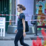 Фотография девушки с татуировкой на предплечье, идущей по улице. На заднем плане видны здания и люди.
