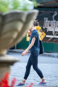 Фотография девушки с татуировкой на предплечье, идущей по улице. Девушка одета в футболку и джинсы, на ногах - кеды.