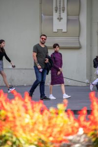 Фото мужчины с татуировкой ворона на предплечье, идущего по улице с женщиной на фоне красных цветов. Детализированный рисунок татуировки.