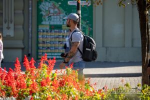 Фото мужчины с татуировкой горного пейзажа на руке, идущего по улице с рюкзаком. Черно-серые тона, реалистичный стиль.
