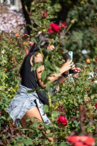 Фотография девушки с татуировкой на плече, стоящей среди цветущих роз. Татуировка выполнена в темных тонах и изображает животное.