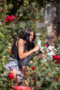Фотография девушки с татуировкой на плече, стоящей среди цветущих роз. Татуировка выполнена в темных тонах и изображает животное.