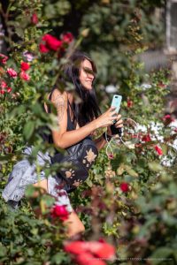 Фотография девушки с татуировкой на плече, стоящей среди цветущих роз. Татуировка выполнена в темных тонах и изображает животное.