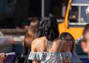 Фотография татуировки на спине девушки. Рисунок выполнен в черном цвете и представляет собой сложный цветочный орнамент. Уличная фотография.