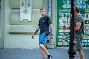 Фотография мужчины с татуировкой на руке, идущего по улице. Татуировка выполнена в черном цвете и покрывает большую часть предплечья. Уличная фотография.