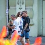 Фото тату на руке мужчины, идущего по улице. Татуировка выполнена в черном цвете и покрывает большую часть предплечья. Уличная фотография.