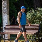 Фото мужчины с татуировкой волка на плече, идущего по парку. Черно-серый рисунок татуировки.