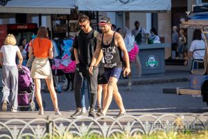 Фото двух мужчин с татуировками на руках, идущих по улице. Видны детали татуировок, включая яркие цвета и необычные рисунки.