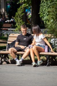 Фотография пары, сидящей на скамейке в парке. У парня заметна татуировка на предплечье, выполненная в темных тонах.