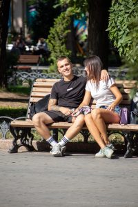 Фотография пары, сидящей на скамейке в парке, где у парня видна татуировка на предплечье.