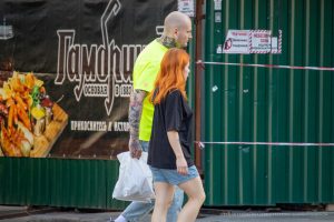 Фото татуировки на руке мужчины, изображающей ворона. Тату выполнено в ярких цветах, с высокой детализацией. Виден городской фон.