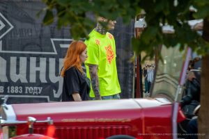 Фото тату: Мужчина в яркой лаймовой футболке с татуировкой волка на плече и рукаве, идущий рядом с рыжеволосой девушкой.