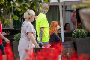 Фото тату: Мужчина с татуировкой волка на руке и глазом на предплечье, разговаривает с женщиной на фоне зелени.