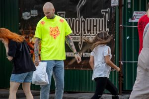 Фото тату: Мужчина в яркой лаймовой футболке с татуировкой волка на плече и рукаве, идущий рядом с девочкой.