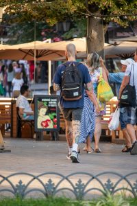 Фотография мужчины с татуировками на руках и ногах, идущего по улице города, с рюкзаком за спиной.