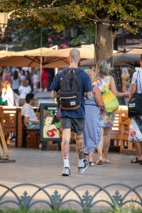 Фото тату на ногах мужчины, идущего по улице. Видны разноцветные рисунки, включая цветы и абстрактные узоры. Стиль татуировки - олдскул.