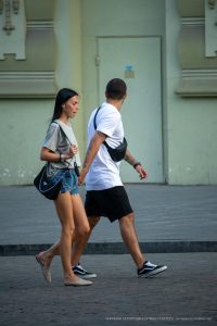 Фотография пары, идущей по улице. У мужчины видна татуировка на руке, а у девушки - на ноге.