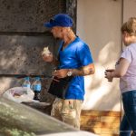 Фотография мужчины с татуировкой на плече, держащего шаурму на улице. Он одет в синюю футболку и кепку.