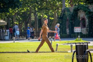 Фото мужчины с татуировкой на руке, гуляющего в парке. Видна часть татуировки с темными контурами. На заднем плане деревья и люди.