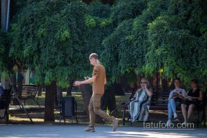Фото тату на плече мужчины, идущего по парку. Видна часть татуировки с изображением животного, выполненной в темных тонах.