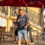 Фотография мужчины с татуировками на руках, стоящего на улице города. Видны татуировки в темных тонах на предплечьях.