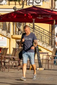 Фотография мужчины с татуировками на руках, стоящего на улице города. Видны татуировки в темных тонах на предплечьях.