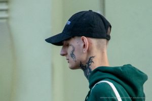 Фотография крупным планом шеи молодого человека с татуировкой в стиле блэкворк, изображающей ветви дерева.