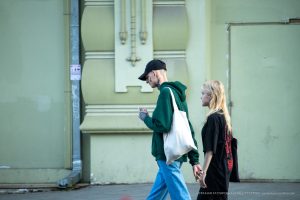 Фотография молодой пары, идущей по улице. У парня видны татуировки на шее и руках, девушка держит сумку.