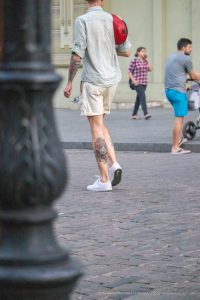 Фотография мужчины, идущего по улице с видимой татуировкой на бедре. Татуировка выполнена в ярких цветах и изображает тигра и цветы.