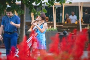 Фото женщины с татуировкой на руке, стоящей на фоне красных листьев. На руке изображен рисунок татуировки в стиле графики.