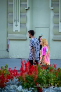 Фото тату: мужчина с татуировкой в стиле аниме на руке, одетый в яркую футболку. Фото сделано на улице.