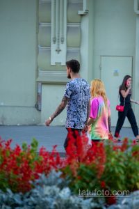 Фото тату: мужчина с татуировкой в стиле аниме на руке, одетый в футболку с аниме-принтом. Фото сделано на улице.