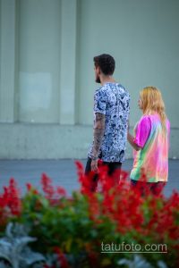 Фото тату: мужчина с татуировкой в стиле аниме на руке, одетый в яркую футболку. Фото сделано на улице.