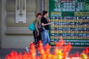 Фото тату на руке: девушка демонстрирует татуировку с растительным орнаментом на фоне яркой городской рекламы. Идеально для вдохновения и поиска идей.