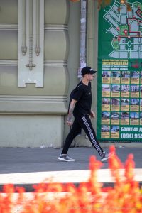 Фотография мужчины в черной кепке и спортивном костюме с татуировкой на предплечье на фоне ярких огней.