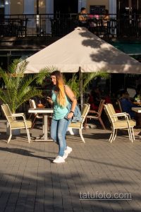Фото татуировки на плече женщины. Виден фрагмент рисунка, предположительно, в стиле графика или орнамента. Черно-серый рисунок на загорелой коже.