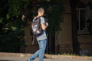 Фото мужчины с татуировкой на руке, идущего по улице с рюкзаком. На руке изображен рисунок татуировки в стиле графики.