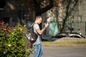 Фото мужчины с татуировкой на руке, идущего по улице с рюкзаком. На руке изображен рисунок татуировки в стиле графики.