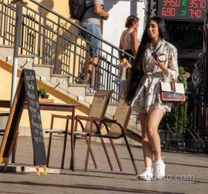 Фотография двух женщин, прогуливающихся по улице, с акцентом на ногу одной из них, украшенную татуировкой с цветами и красными мазками.