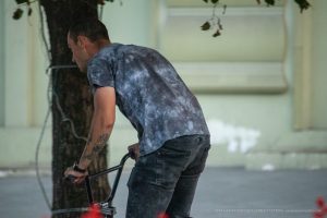 Фото БМХ-райдера с татуировками на руках, наклонившегося над велосипедом. Видны детализированные рисунки татуировок, включая ворона и черепа.