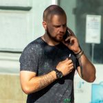 Фото мужчины с татуировками на руках, говорящего по телефону. Видны детализированные рисунки татуировок, включая черепа и другие символы.