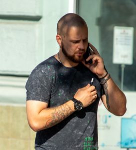 Фото мужчины с татуировками на руках, говорящего по телефону. Видны детализированные рисунки татуировок, включая черепа и другие символы.