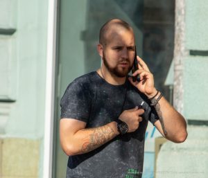 Фото мужчины с татуировками на руках, говорящего по телефону. Видны детализированные рисунки татуировок, включая черепа и другие символы.