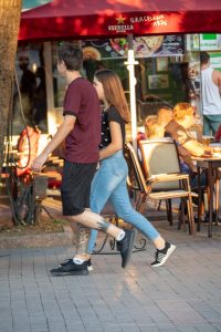 Фотография татуировки в стиле блэкворк на икре ноги парня, идущего с девушкой по улице.